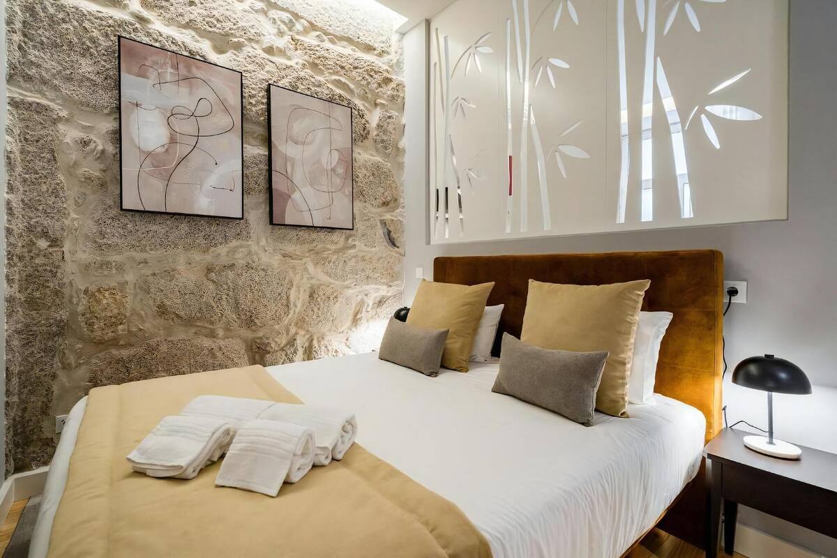 A bed with white linens, a wooden headboard, and a nightstand with a lamp.