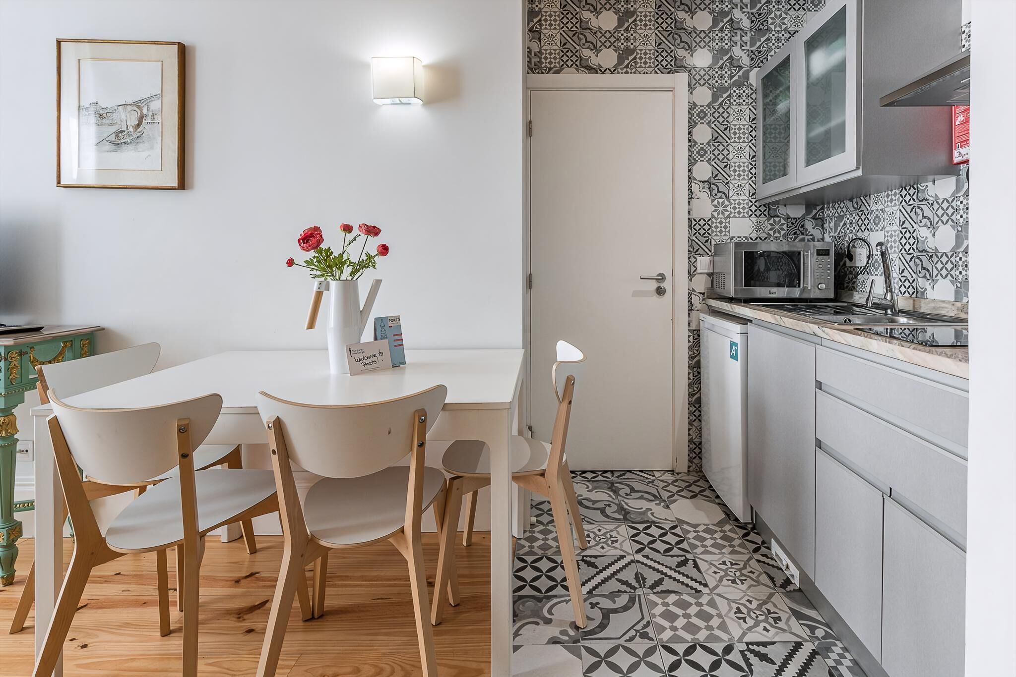Un coin repas avec une table et des chaises blanches, un vase rempli de fleurs et un tableau encadré accroché au mur.