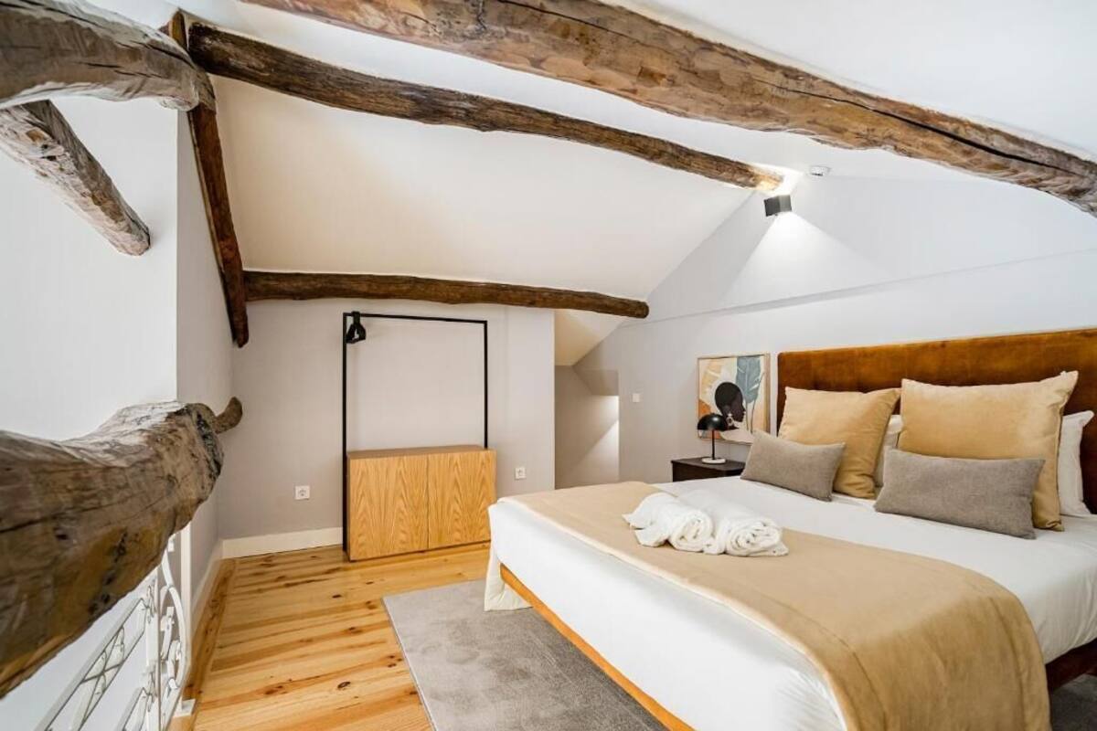 A bedroom with a wooden ceiling, a bed with beige bedding, a nightstand, and a mirror.