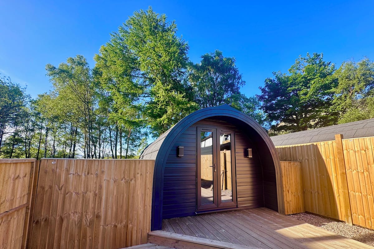 Une cabane en bois avec un toit incurvé, une terrasse en bois et une vue sur les arbres.