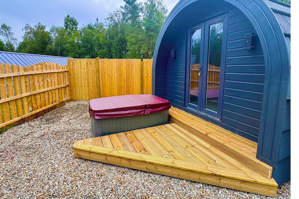 Une petite structure de couleur sombre, dotée d’un toit incurvé, d’une terrasse en bois et d’un banc rouge.