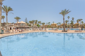 A pool area with lounge chairs, palm trees, and buildings in the background. - Marvin Home in Corralejo: Renovated Apartment with Garden View (Corralejo)