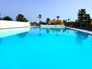 A clear blue swimming pool with a white wall on one side and a yellow building in the background.