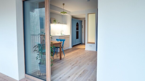 Una cocina moderna con suelo de madera, un armario azul y una zona de comedor con mesa y sillas.