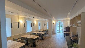 Un comedor espacioso con mesas y sillas largas, iluminación colgante y vistas al exterior.