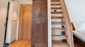 Una escalera de madera conduce a un dormitorio en buhardilla con techo inclinado y vigas a la vista.
