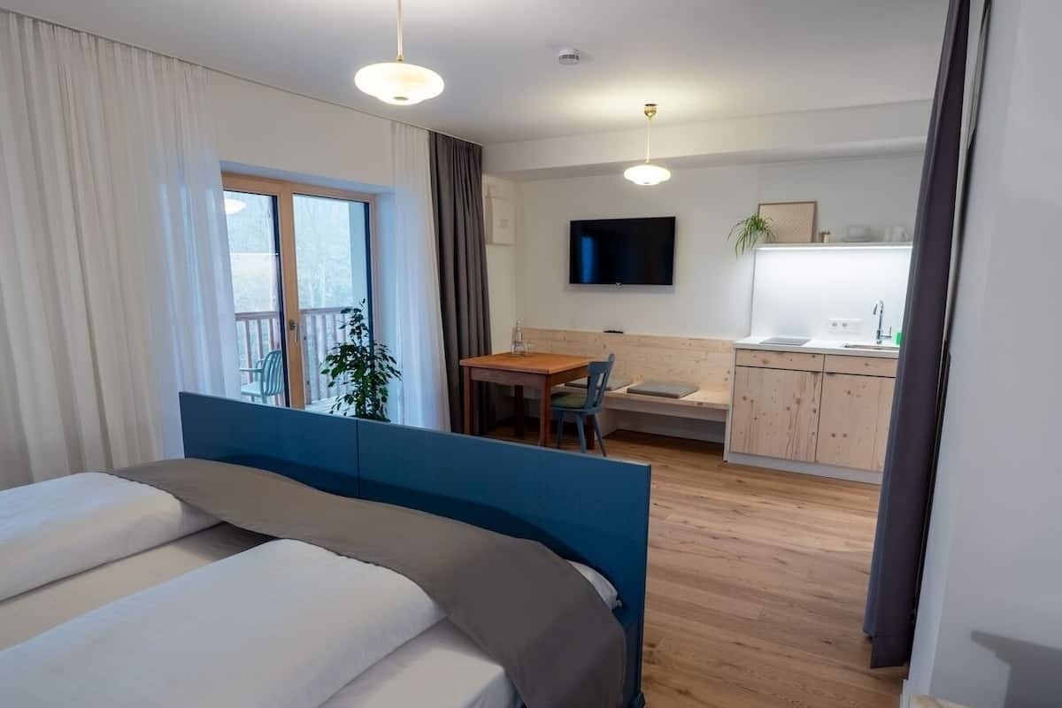 Une chambre d’hôtel avec un grand lit, un bureau, une chaise, une télévision et une kitchenette.
