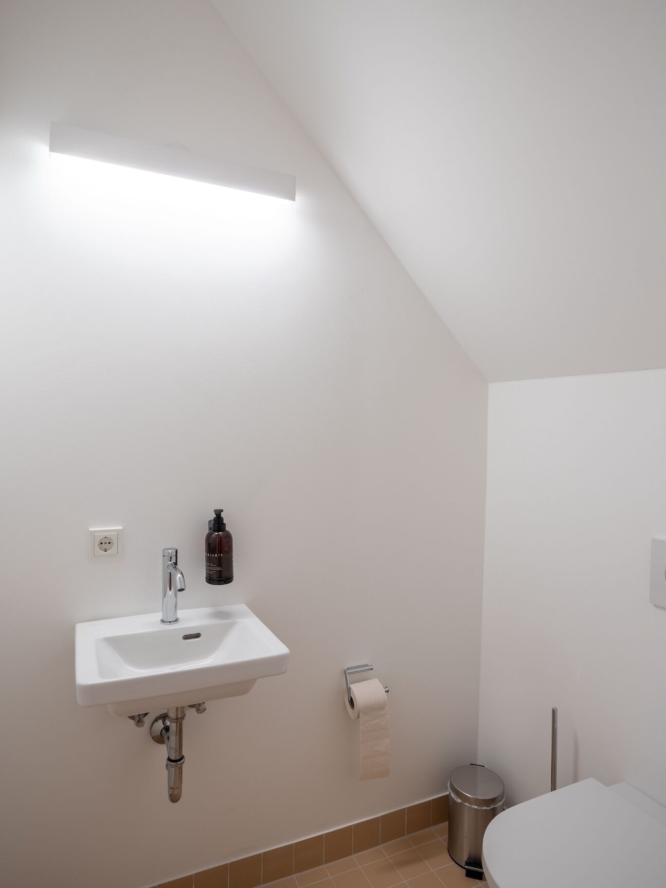 A bathroom with a white sink, a toilet, and a trash can.