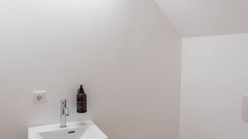 A bathroom with a white sink, a toilet, and a trash can.