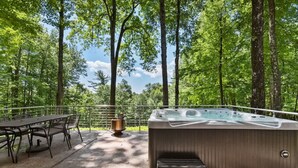 Eine Außenpatio mit Whirlpool, Tisch und Stühlen, umgeben von Bäumen.