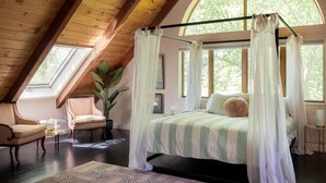 A bedroom with a canopy bed, a sitting area with a chair and table, and large windows with a view of trees. - Catskill Estate w Epic Views hot tub (Kingston)