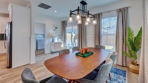 A modern dining area with a wooden table, grey upholstered chairs, and a chandelier. - Dreamland (Wilmington)