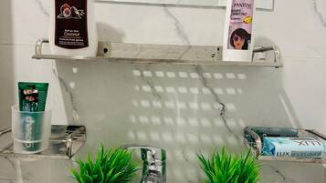 Un baño con un lavamanos blanco, dos plantas verdes, un dispensador de jabón para manos y una botella de champú.