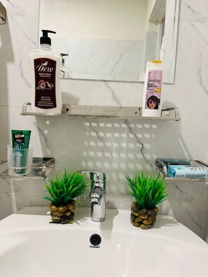 Un baño con un lavamanos blanco, dos plantas verdes, un dispensador de jabón para manos y una botella de champú.