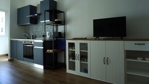 A modern kitchen with a built-in oven, a microwave, and a coffee machine. There is a black TV on a wooden shelf, and a white cabinet with glass doors. - Grimani Suite (Milan)