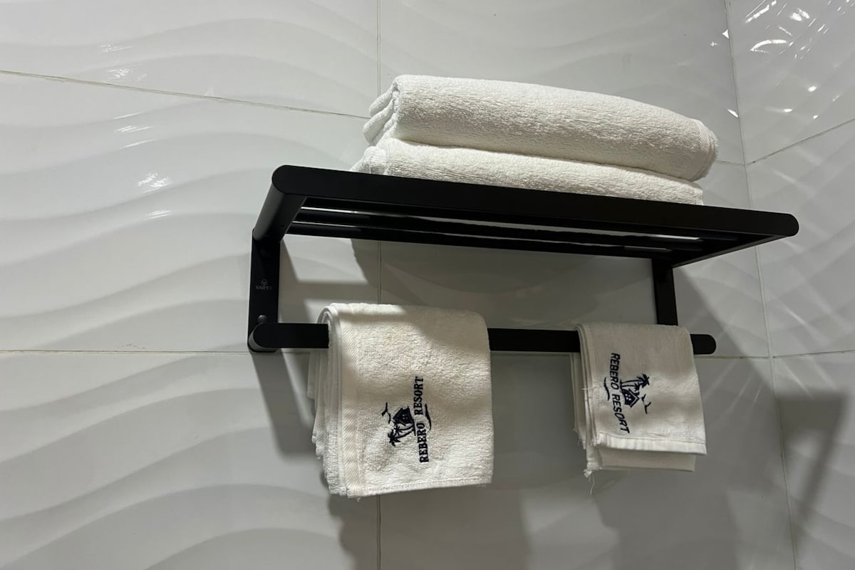 A black towel rack with two folded towels and one rolled towel against a white tiled wall.