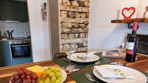 A dining table with plates of food, wine, and glasses, a kitchen in the background, and a decorative wall.