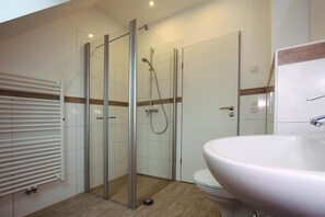 Ein modernes Badezimmer mit einer Duschkabine, einem weißen Waschbecken und einer Toilette.