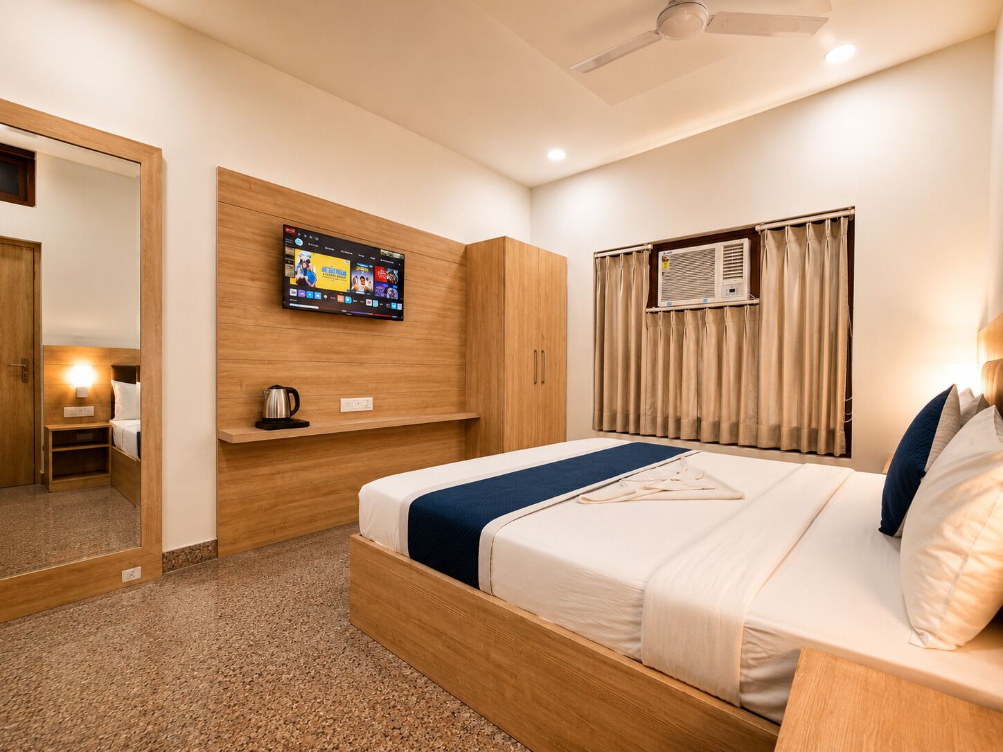 Habitación de hotel con cama, televisión montada en la pared, ventilador de techo y aire acondicionado.