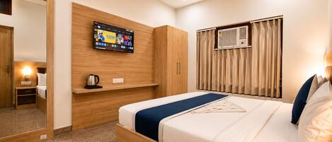 Habitación de hotel con cama, televisión montada en la pared, ventilador de techo y aire acondicionado.