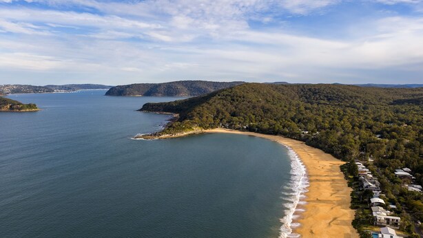 Eine Küstenlandschaft mit Sandstrand, bewaldeten Hügeln und freiem Blick auf den Ozean.