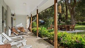Eine überdachte Terrasse mit Gartenmöbeln, einer Ziegelwand und einem Gartenbereich mit Pflanzen und einem Baum.