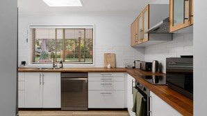Eine moderne Küche mit weißen Schränken, einem Geschirrspüler, einer Holz Arbeitsplatte, einem Fenster mit Jalousien und einem eingebauten Backofen.