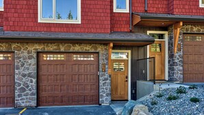 A two-story house with a stone facade, a wooden front door, and two garage doors.