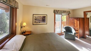 Une chambre d’hôtel avec un grand lit, une chaise, un bureau avec une lampe, un tableau encadré au mur et une porte coulissante donnant sur un balcon.