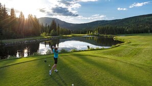 A golf course with a pond, trees, and a mountain in the background. - Modern Open Concept 2 bedroom Ski In/Ski Out Bottom Floor Unit! (Sun Peaks)