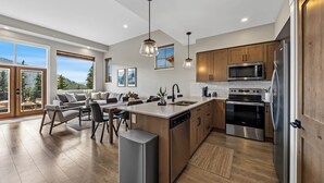 Una cocina moderna con una isla central, electrodomésticos de acero inoxidable, armarios de madera y ventanas amplias con vistas al exterior.