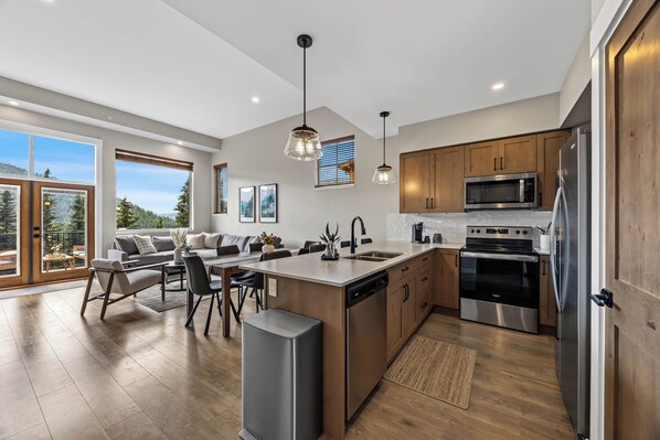 A modern kitchen with a central island, stainless steel appliances, wooden cabinets, and large windows offering a view of the outdoors.