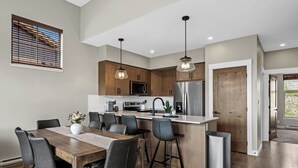 Una cocina moderna con armarios de madera, un refrigerador de acero inoxidable y un comedor con una mesa y sillas de madera.