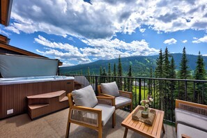 A balcony with wooden furniture, a hot tub, and a view of mountains and trees.