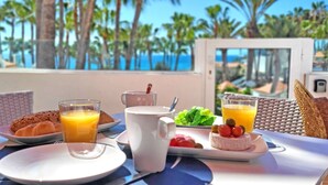 A breakfast table with plates of food, glasses of orange juice, and a view of palm trees and the ocean. - Vacation apartment EL PARAISO in Costa Calma, close to the beach, pool, terrace (Costa Calma)