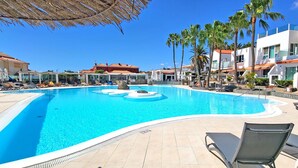A swimming pool with lounge chairs, palm trees, and modern buildings in the background. - Vacation apartment EL PARAISO in Costa Calma, close to the beach, pool, terrace (Costa Calma)