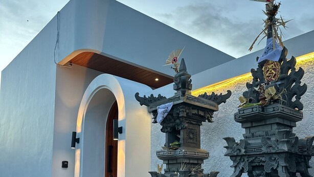 Un edificio moderno con fachada blanca, una puerta de madera y dos estructuras de piedra intrincadamente talladas con diseños tradicionales.