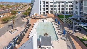 A modern hotel with a rooftop pool, outdoor seating, and a view of a bridge and mountains.
