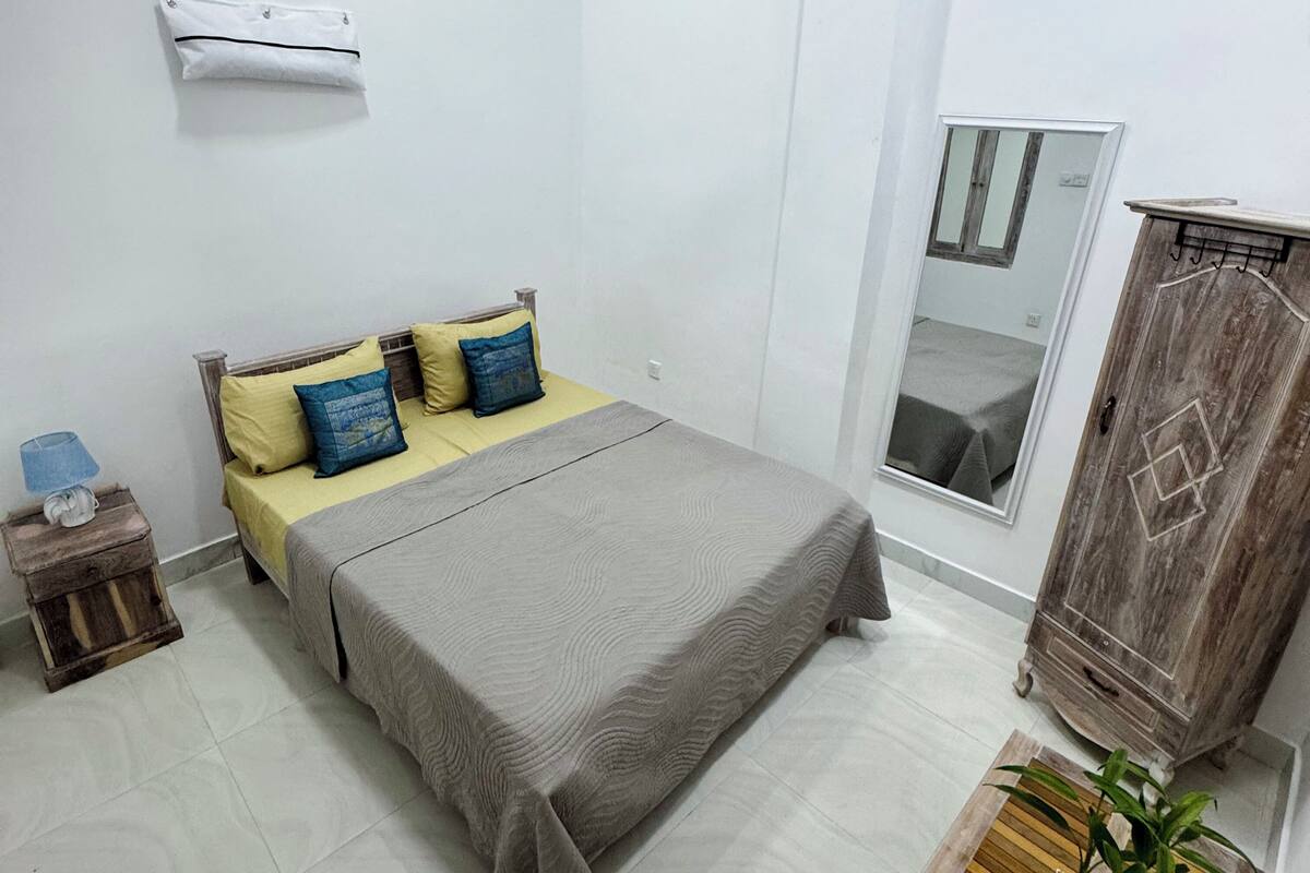 Un dormitorio con cama, mesita de noche, espejo, armario y una planta en maceta.