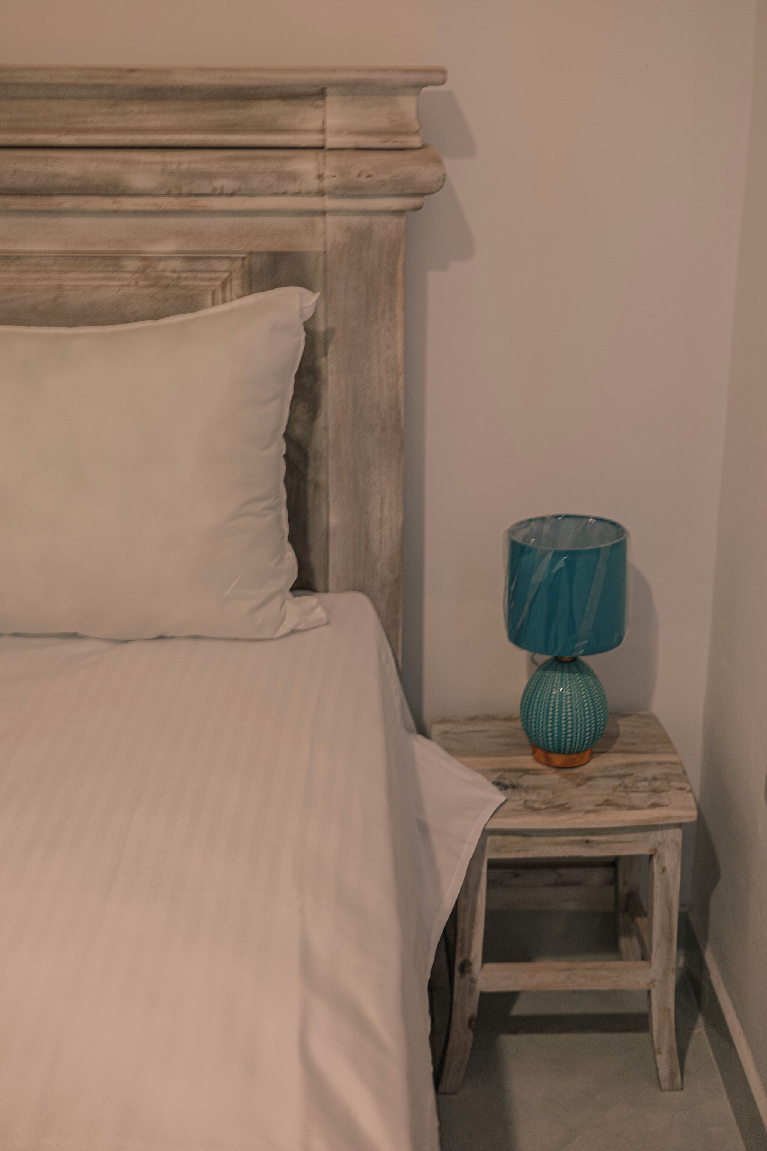 Un letto con testiera in legno e un comodino con lampada color petrolio.