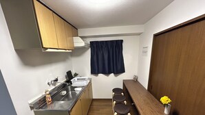A compact kitchen with a sink, cabinets, a countertop, and a wooden table with stools.