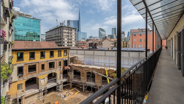 Bybillede med moderne bygninger, en byggeplads og et overdækket gangareal.