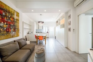 A modern living room with a sofa, ottoman, and a dining area with a table and chairs.