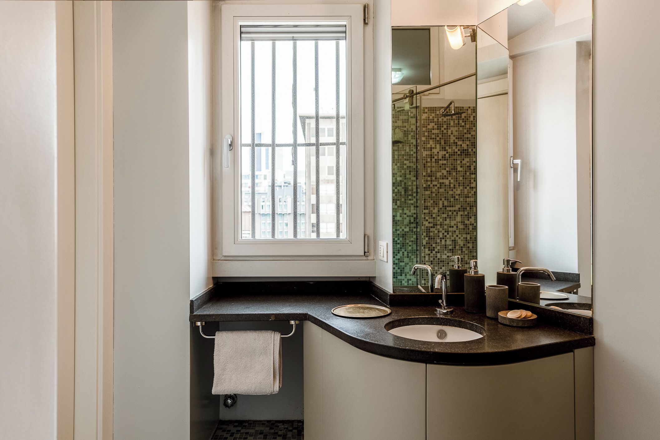 A modern bathroom with a curved sink, a glass shower enclosure, and a window providing natural light.