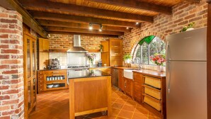 Een keuken met een bakstenen muur, houten kastjes, een roestvrijstalen fornuis en een groot raam met uitzicht op groen.