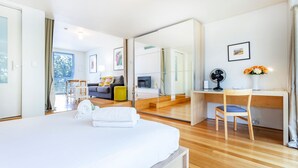 A modern hotel room with a large bed, a desk, a chair, a mirror, and a view of the outdoors. - Cottesloe Tree Top Studio (Cottesloe)