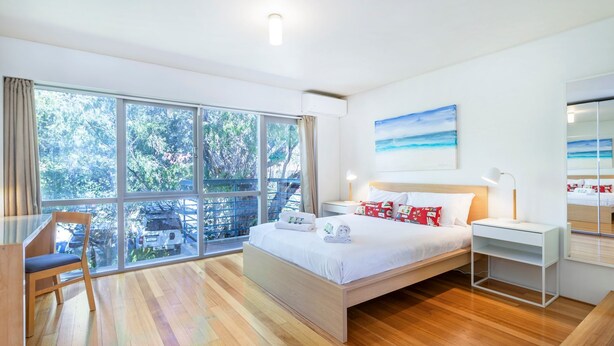 A modern hotel room with a large bed, a desk, a chair, and a balcony with a view of trees and a car. - Cottesloe Tree Top Studio (Cottesloe)