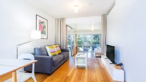 A modern living room with a sofa, a coffee table, a TV, and a dining area. - Cottesloe Tree Top Studio (Cottesloe)