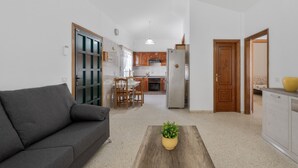 Una sala de estar con sofá, una mesa de centro con una planta, una cocina al fondo y puertas de madera.