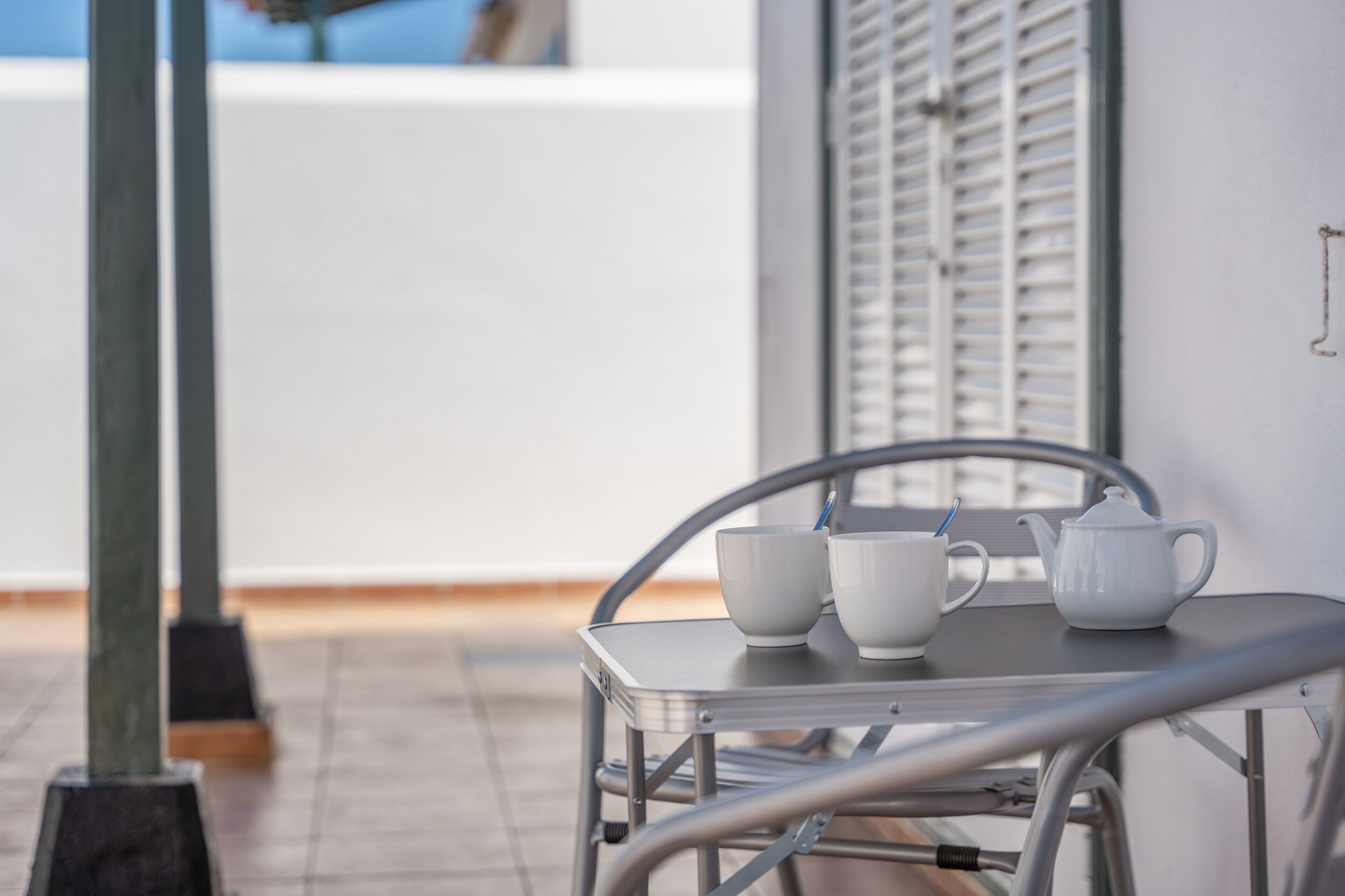 Une table en métal avec deux tasses blanches et une théière, sur un balcon.